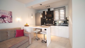 Una cocina moderna con encimera blanca, electrodomésticos de acero inoxidable y una zona con taburetes de bar.