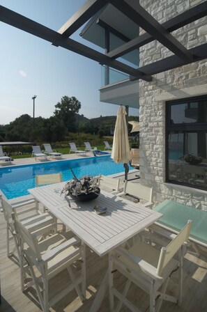 A poolside area with a table and chairs, a stone wall, and a view of the pool.