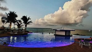 A pool area with palm trees, a small structure, and a view of the ocean. - Morritts Tortuga Club (East End)