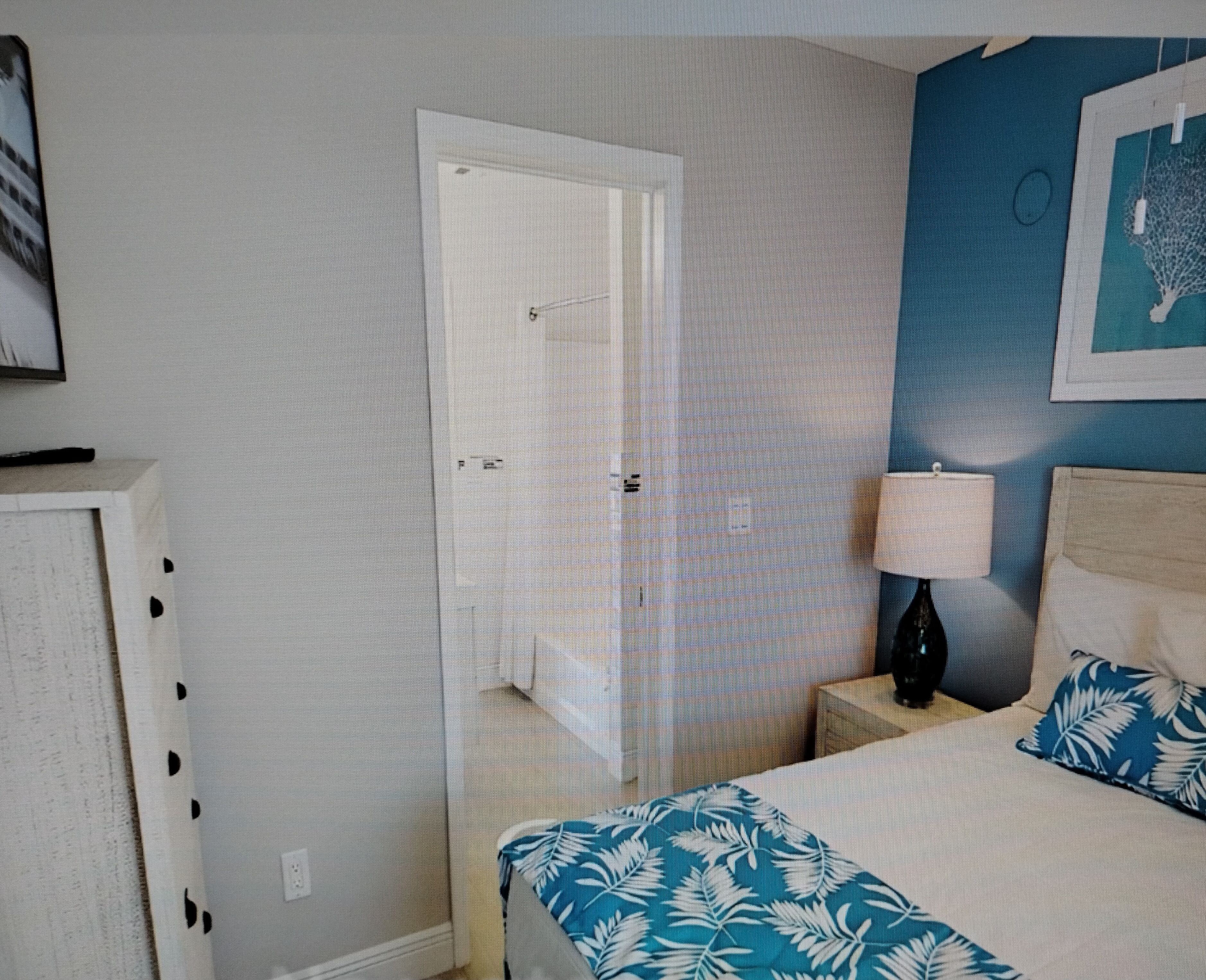 A bedroom with a bed, a nightstand, a lamp, a door, and a wall with a painting.