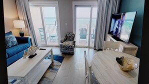 A living room with a blue sofa, a coffee table, a TV, and a view of the ocean through large windows. - Morritts Tortuga Club (East End)