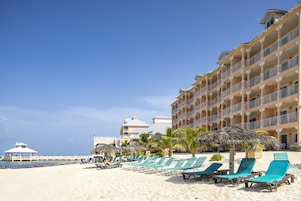 Una playa con sillas de descanso y un hotel al fondo.