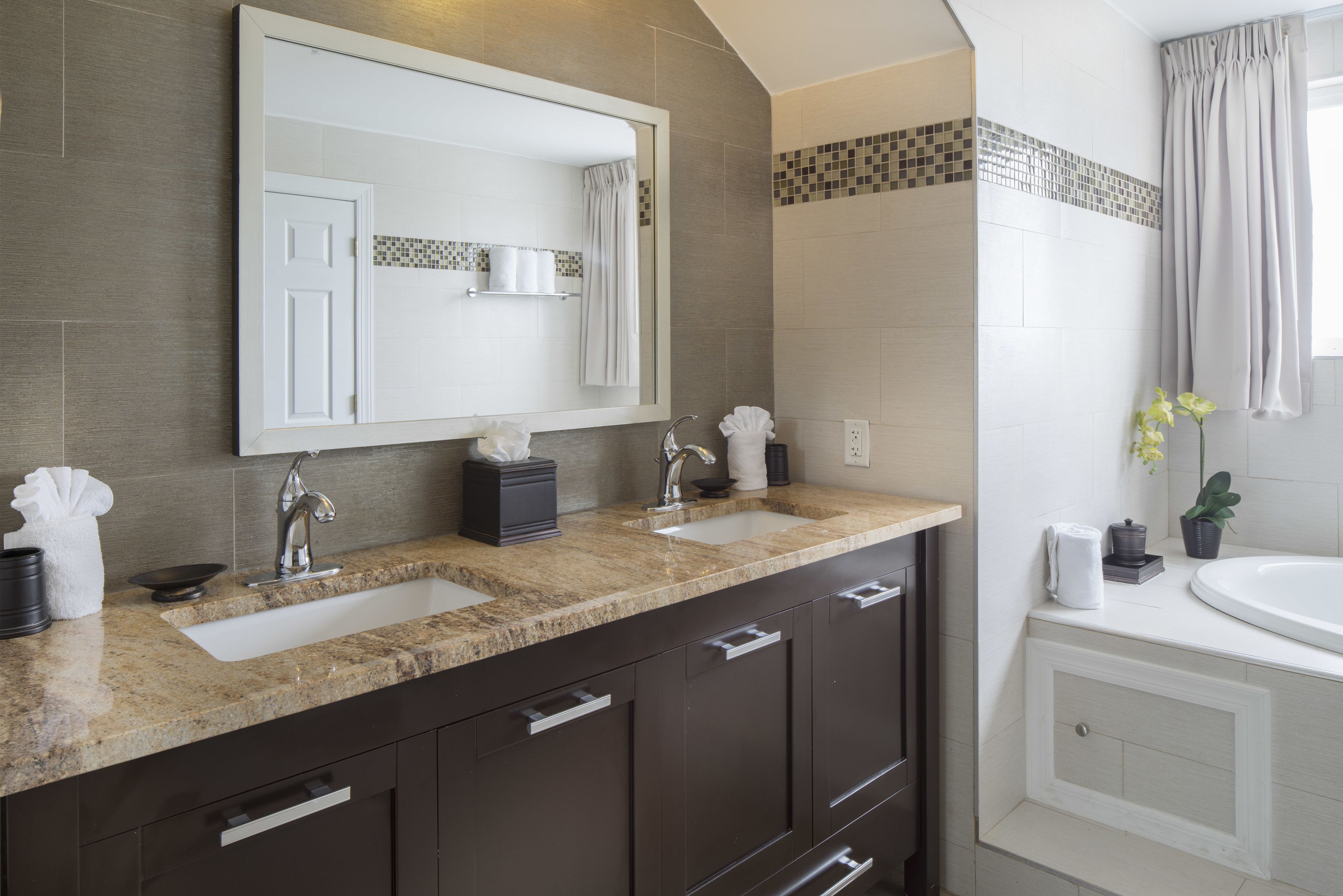 A modern bathroom with two sinks, a large mirror, and a bathtub.