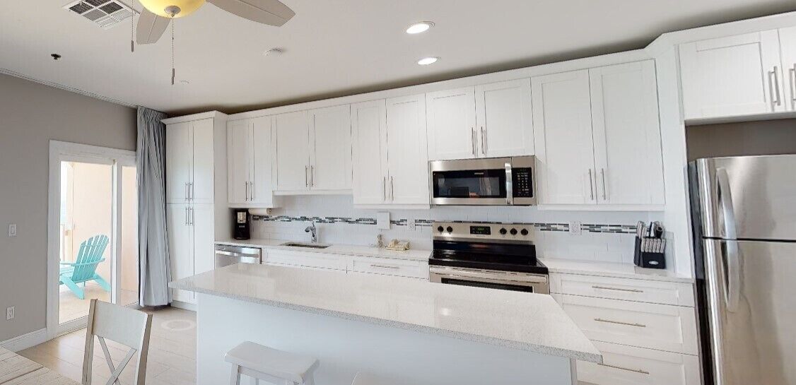A modern kitchen with white cabinets, stainless steel appliances, and a large island.