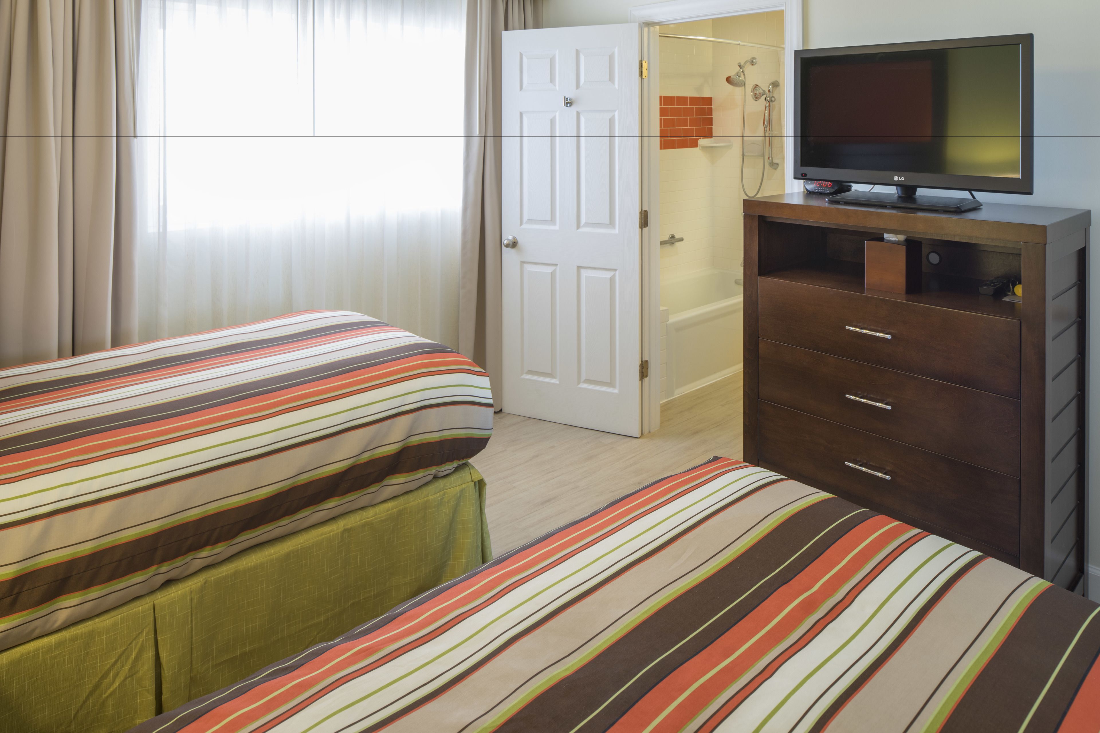 Habitación de hotel con dos camas, un televisor sobre una cómoda y la puerta del baño.