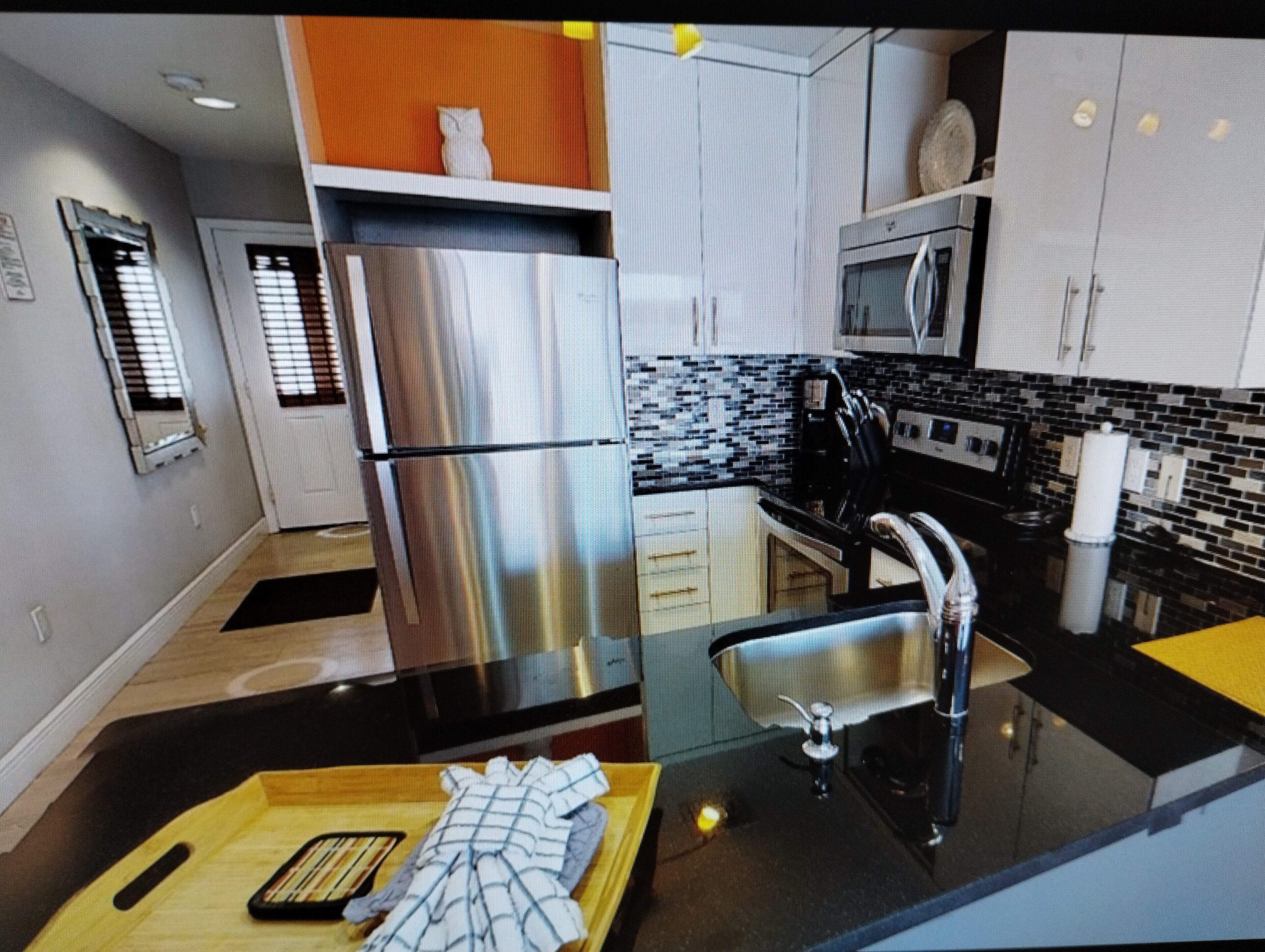 Cozinha moderna com eletrodomésticos de aço inoxidável, bancada preta e painel de azulejos.