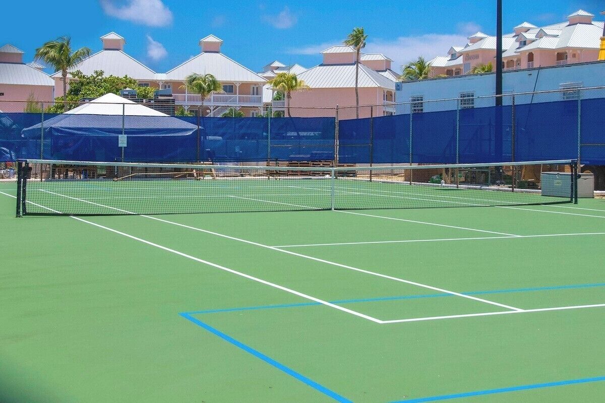 A tennis court with a net, surrounded by a fence and covered by a blue canopy.