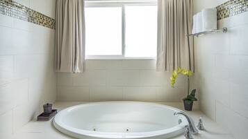 Un baño con una bañera grande, una ventana con cortinas, un perchero para toallas y una pequeña planta en maceta.