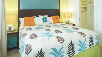 A neatly made bed with a leaf-patterned bedspread, two bedside lamps, a nightstand, and a green drawer unit.
