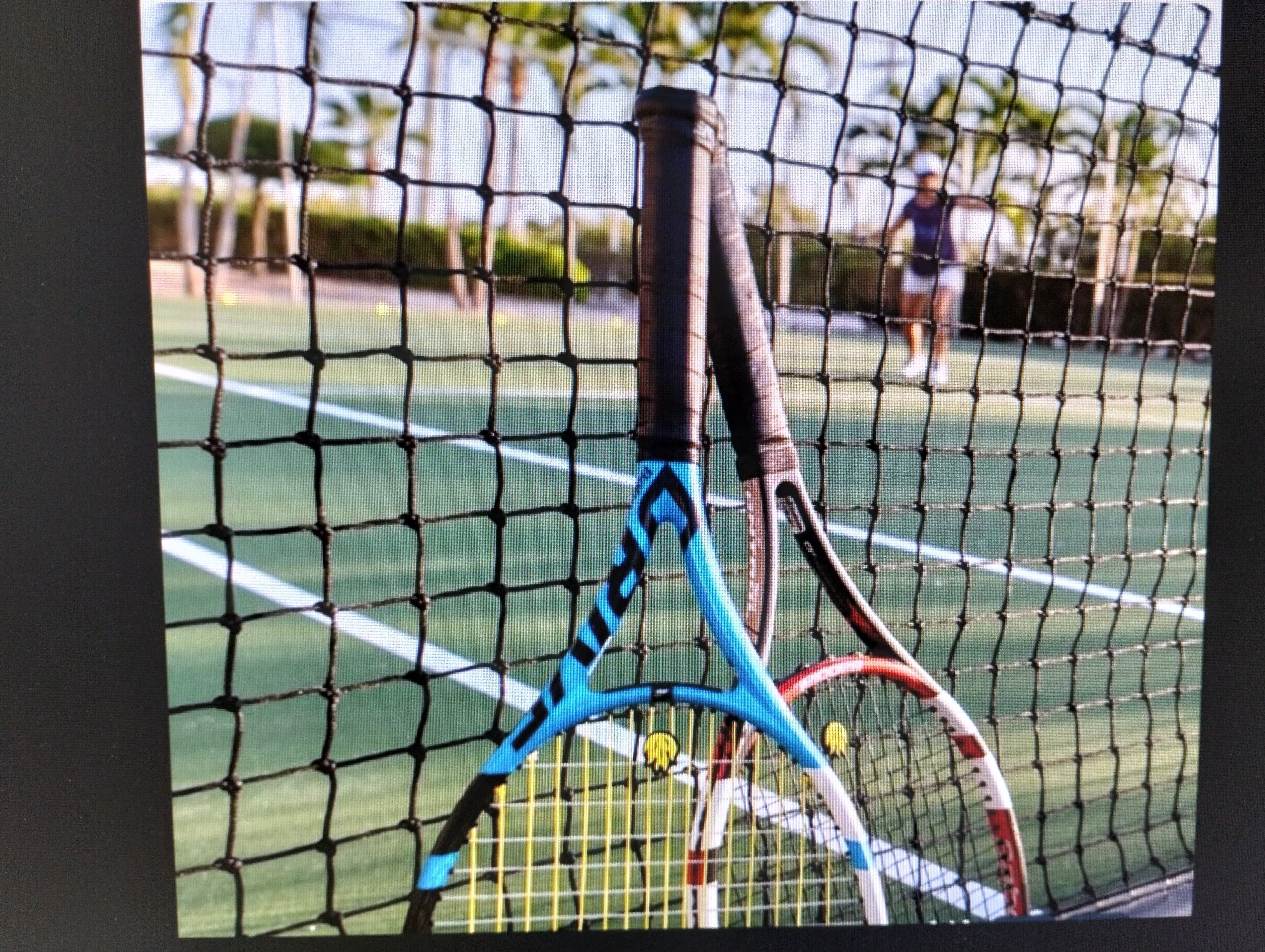 Un court de tennis avec un filet au premier plan et un joueur en arrière-plan.