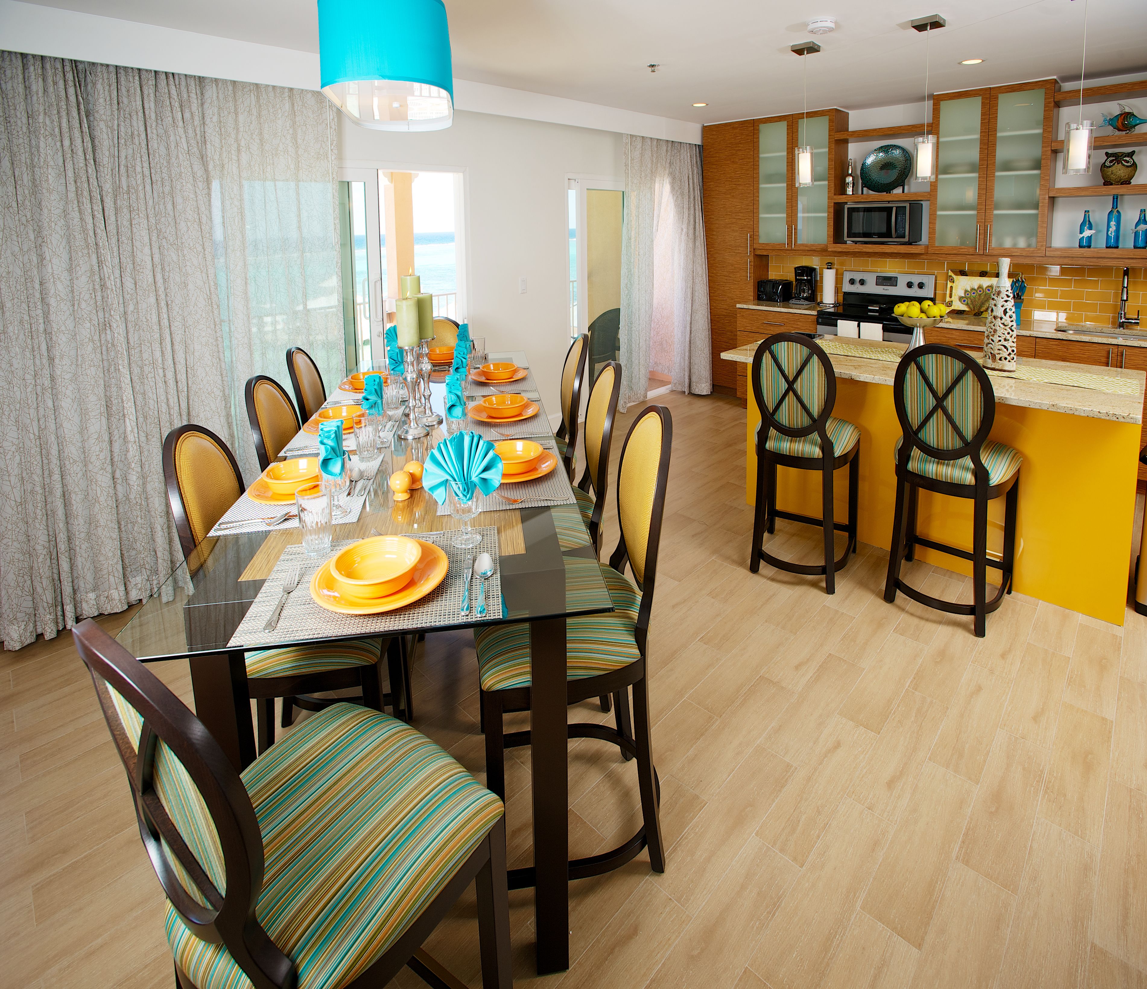 A modern dining area with a glass table, striped chairs, and a kitchen in the background.