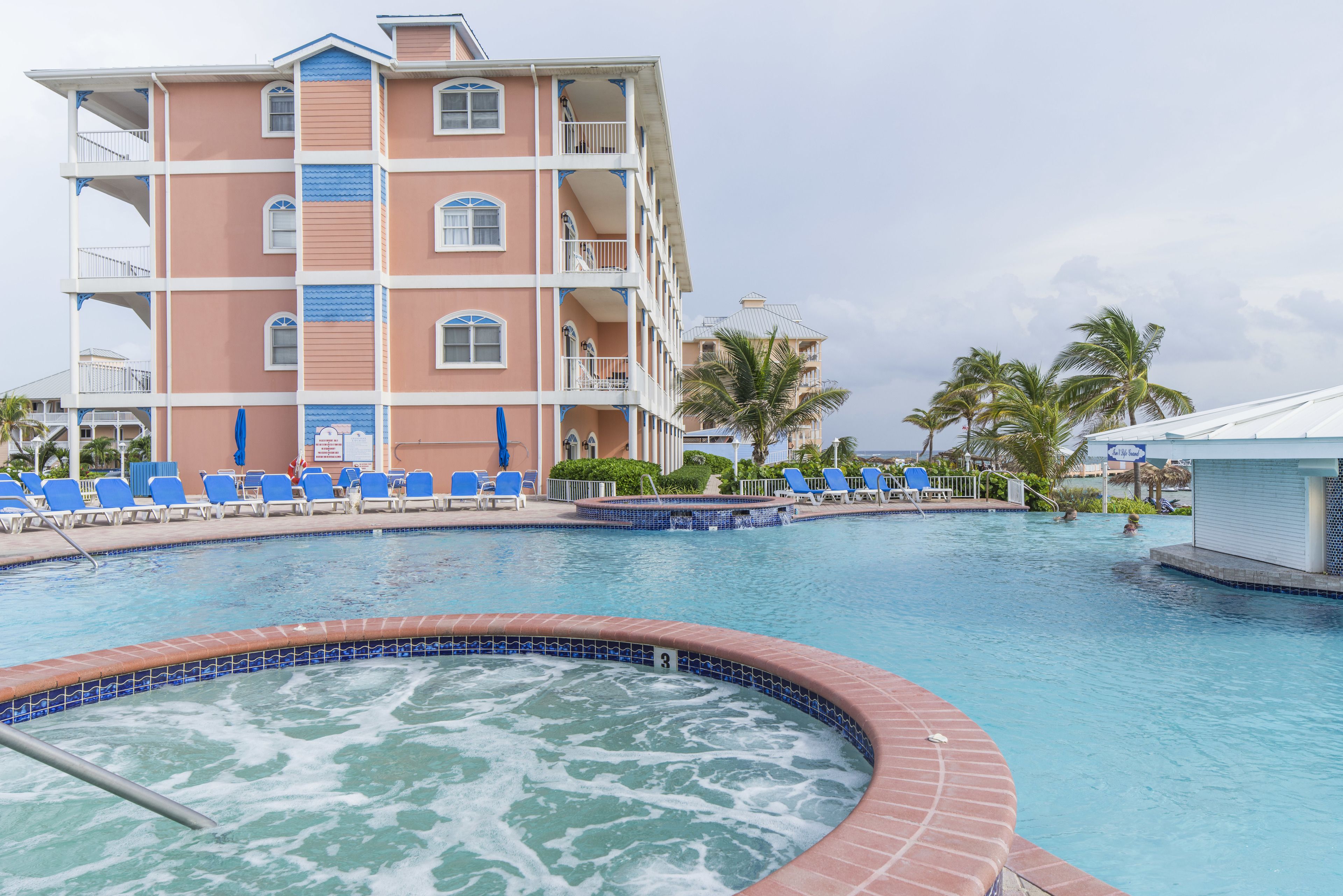 A hotel with a swimming pool, multiple balconies, and lounge chairs.