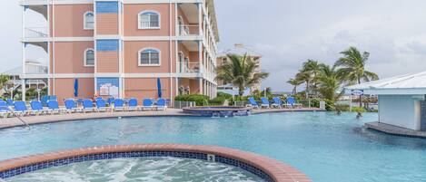 A hotel with a swimming pool, multiple balconies, and lounge chairs.