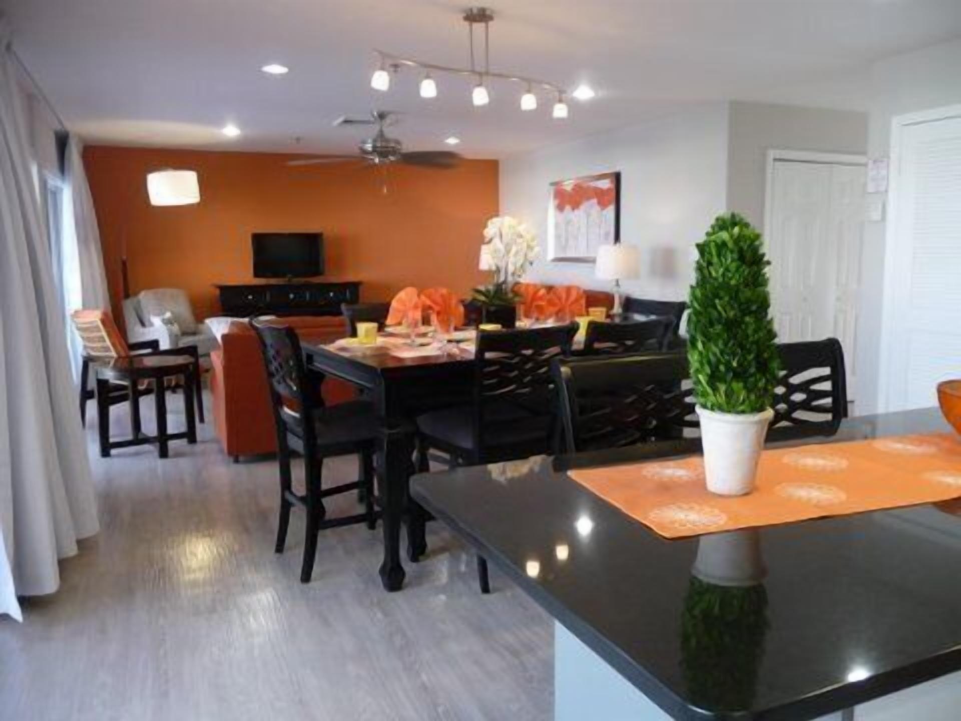 A modern dining area with a black table, orange placemats, and a potted plant.