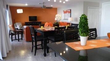 Un comedor moderno con una mesa negra, individuales naranja y una planta en maceta.