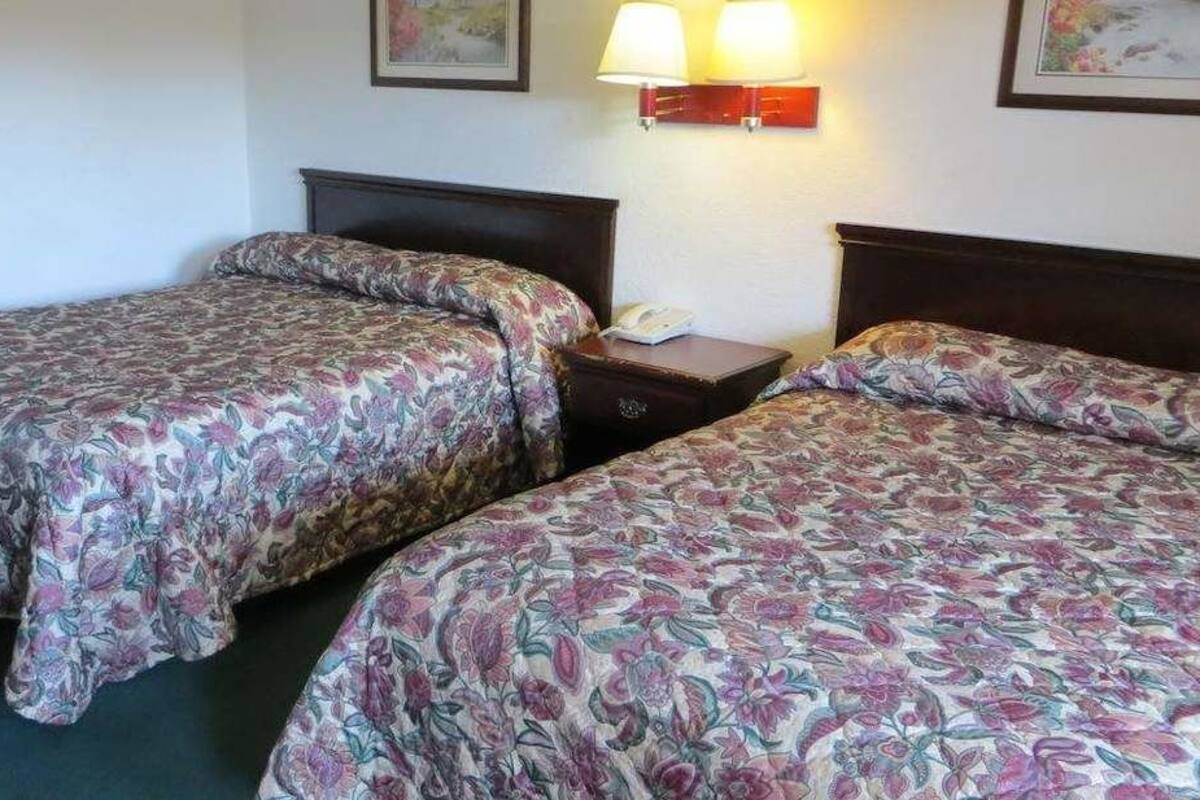 A hotel room with two beds, each with floral-patterned bedding, a nightstand with a lamp, and a framed picture on the wall.