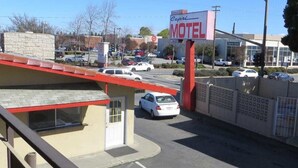 A motel with a red roof, a white car parked in front, and a sign for 'Capri Motel' in the background. - Capri Motel (Redwood City)