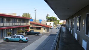 A motel with a row of rooms, a parking lot, and a building with a red roof. - Capri Motel (Redwood City)
