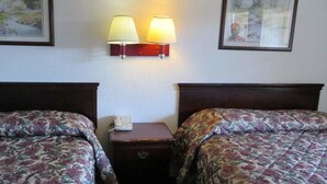 A hotel room with two beds, a nightstand with a lamp, and framed artwork on the walls. - Capri Motel (Redwood City)