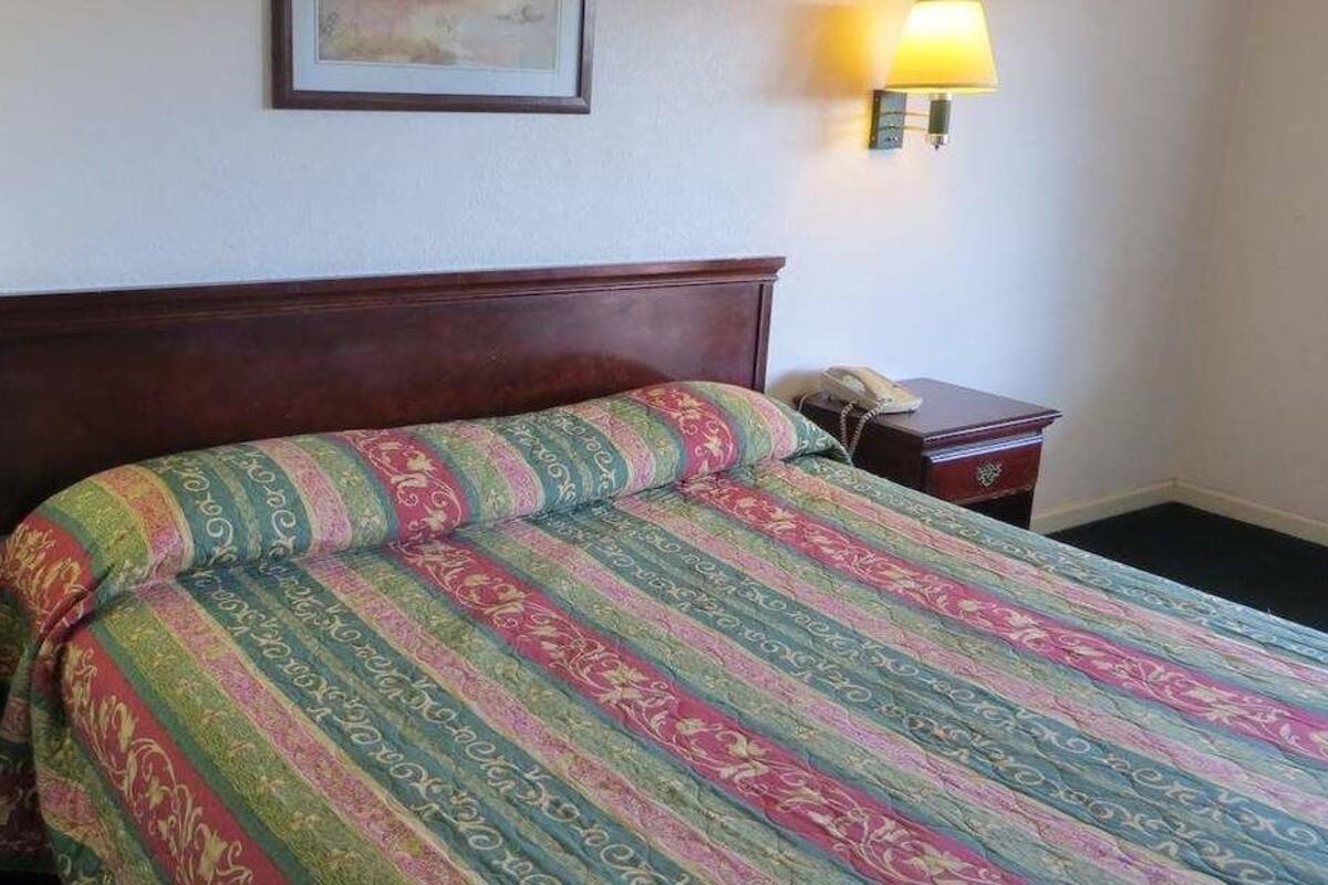 A neatly made bed with a patterned bedspread, a bedside table with a lamp, and a wall-mounted telephone.