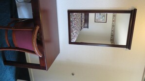 A room with a wooden dresser, a chair, and a wall-mounted mirror. - Capri Motel (Redwood City)
