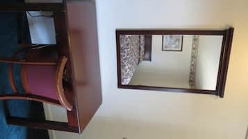 Una habitación con un aparador de madera, una silla y un espejo fijado a la pared.