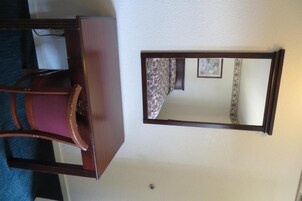 Una habitación con un aparador de madera, una silla y un espejo fijado a la pared.