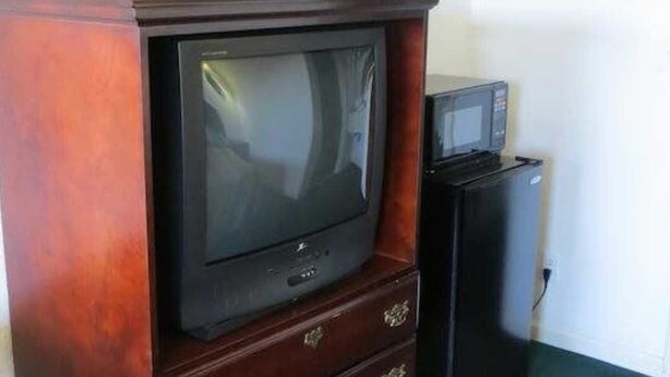 A television set on a wooden cabinet with a microwave on top. - Capri Motel (Redwood City)