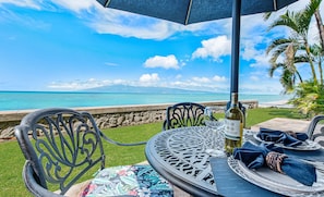 Enjoy a serene ocean view from this outdoor dining area, featuring a round table and two chairs.