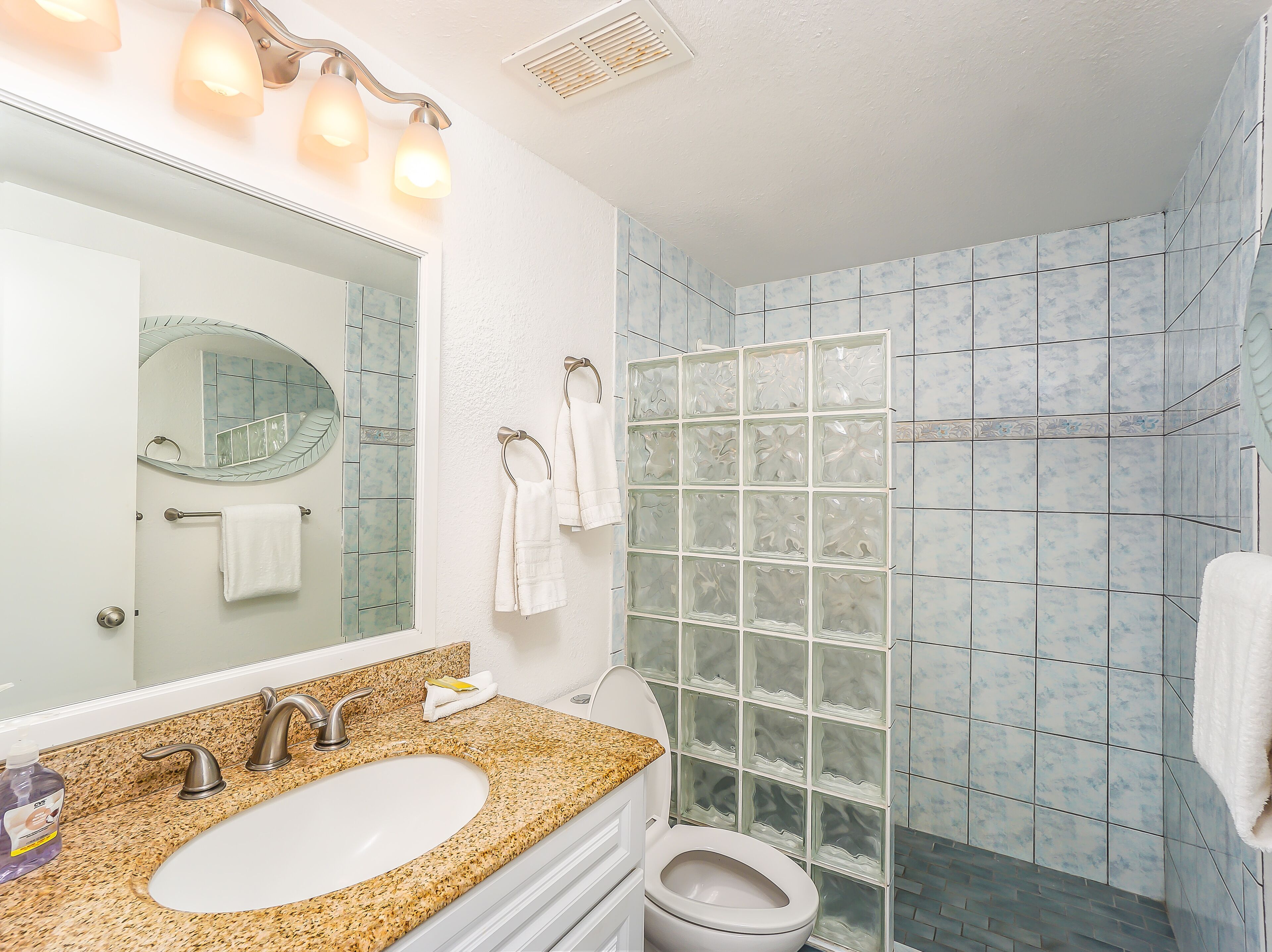 A bathroom with a granite countertop sink, a mirror, a towel rack, and a glass shower enclosure.