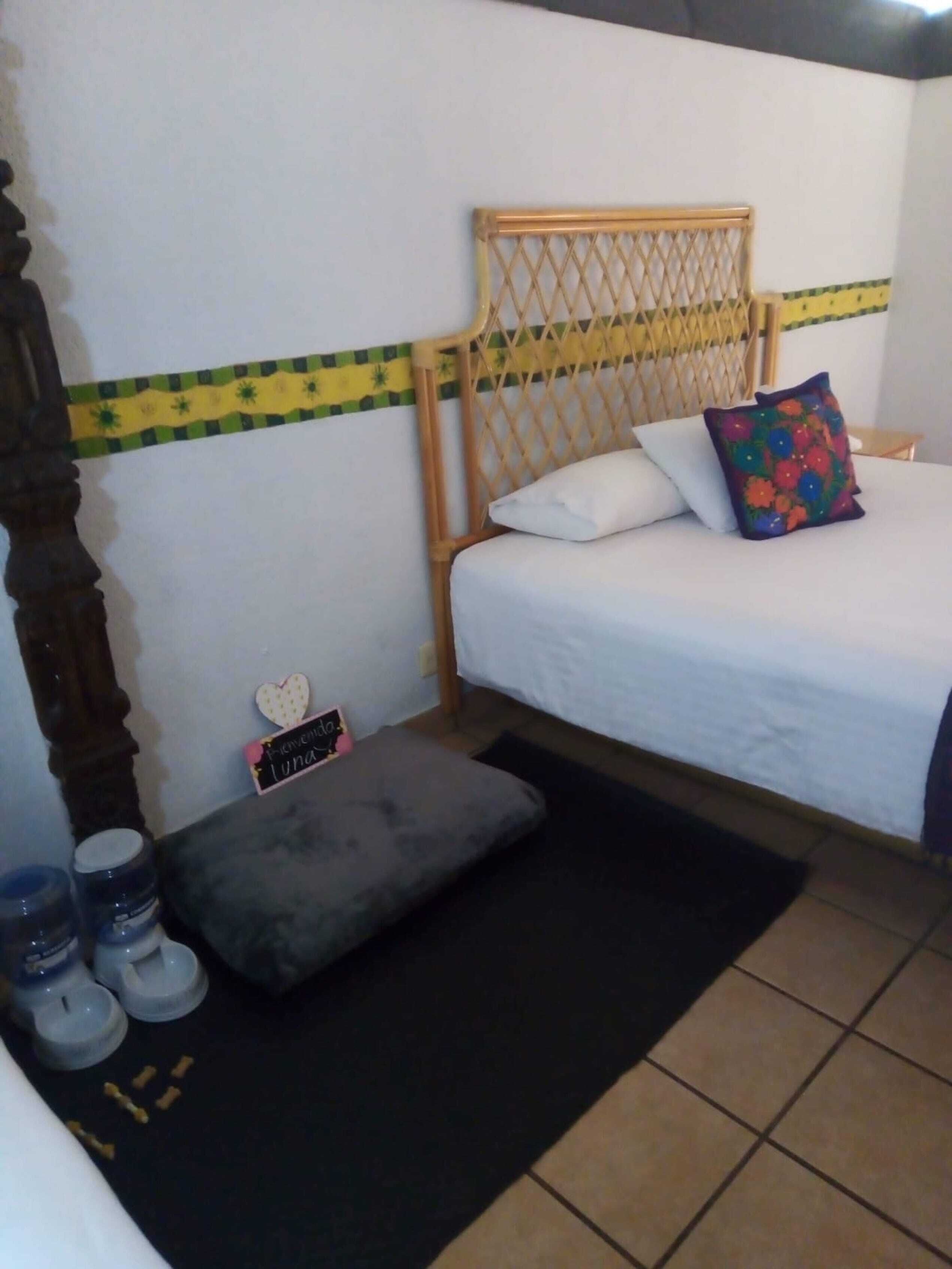 A bedroom with a bed, a wooden headboard, a small bedside table, a pillow, a bedside lamp, and a black rug.