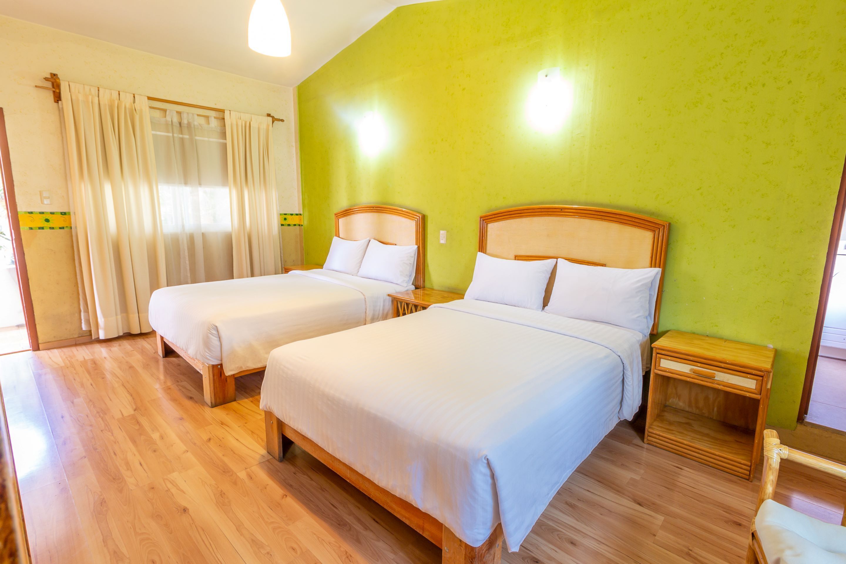A room with two beds, wooden flooring, and a green wall.