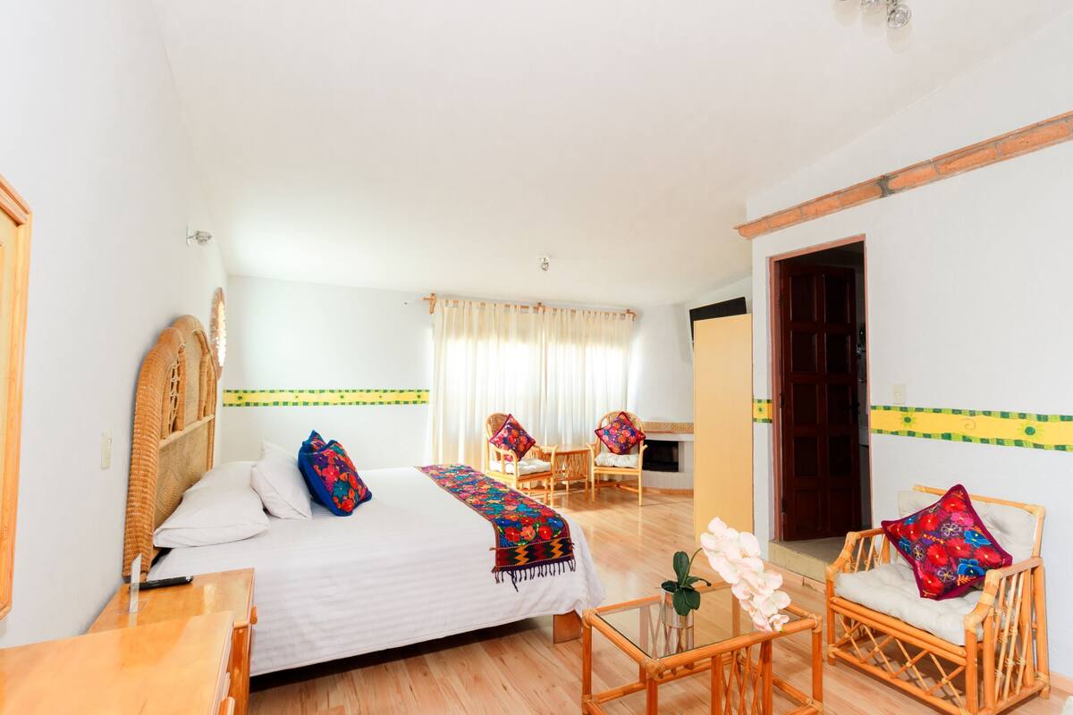 A hotel room with a bed, two chairs, a small table, and a window with curtains.