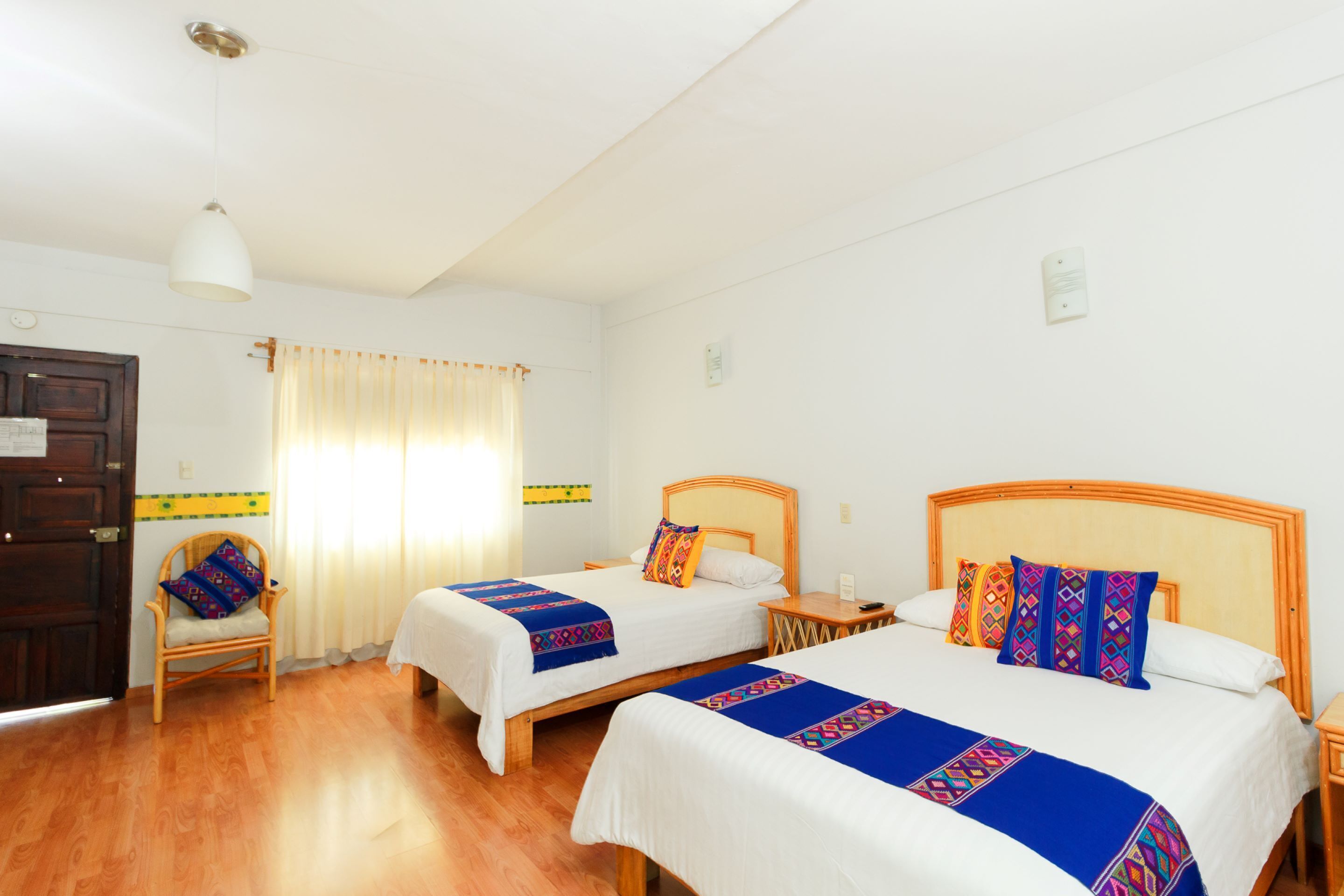 Una habitación de hotel con dos camas, una silla, una mesita de noche y suelo de madera.