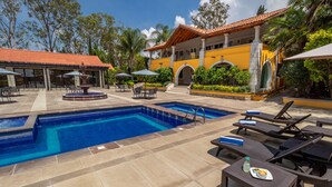 A pool area with lounge chairs and umbrellas, a fountain, and a building with a tiled roof. - Hotel Hacienda Montesinos (Morelia)