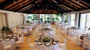 A spacious hall with multiple round tables set for dining, white chairs, and large windows allowing natural light. - Hotel Hacienda Montesinos (Morelia)