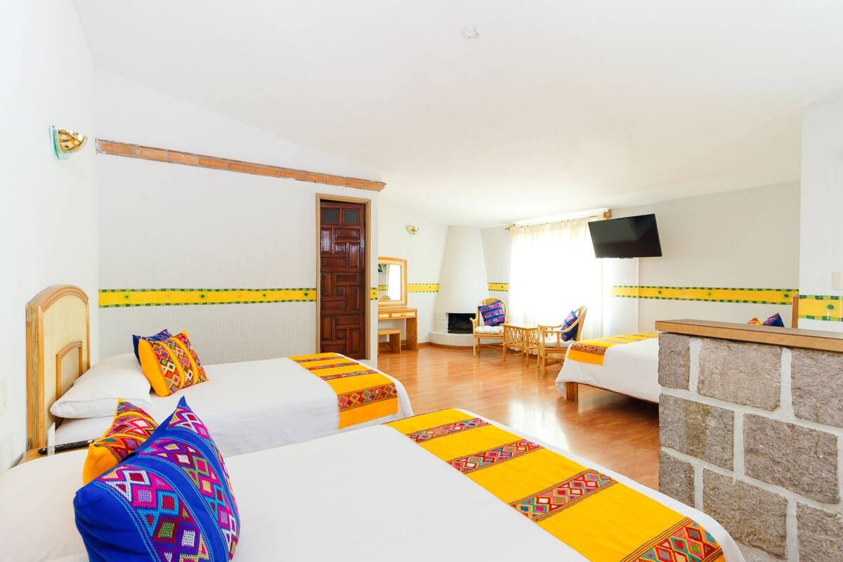 A hotel room with two beds, a desk, a chair, a television, and a stone wall.