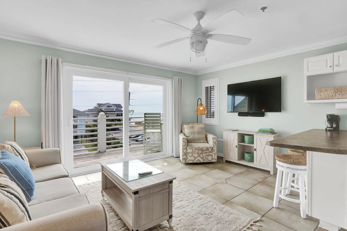 Un salon comprenant un canapé, une table basse, un téléviseur, un ventilateur de plafond et une vue sur l’extérieur.