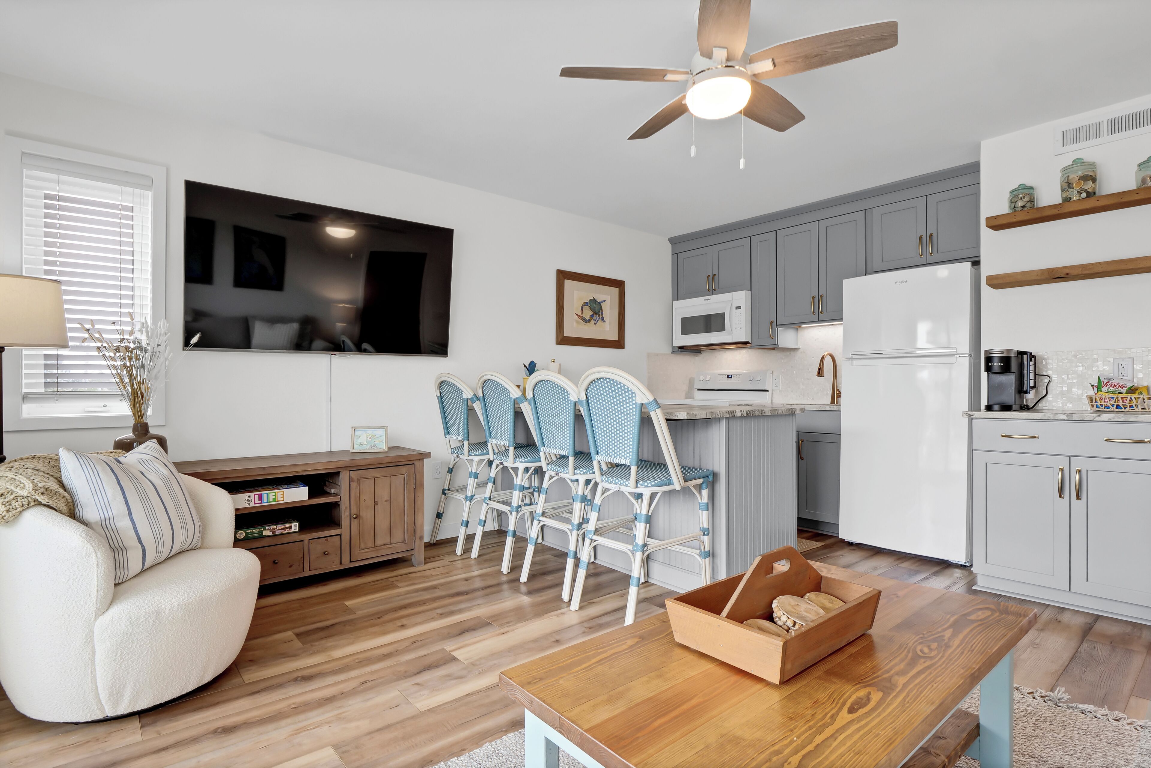 A modern kitchen with grey cabinets, a white refrigerator, and a wooden dining table with chairs.