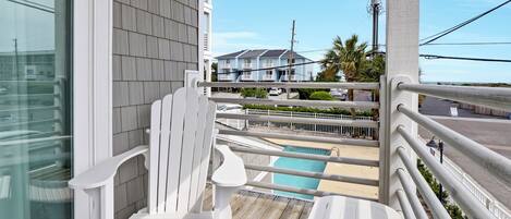 A wooden deck with a white chair and table, overlooking a swimming pool and a residential area.