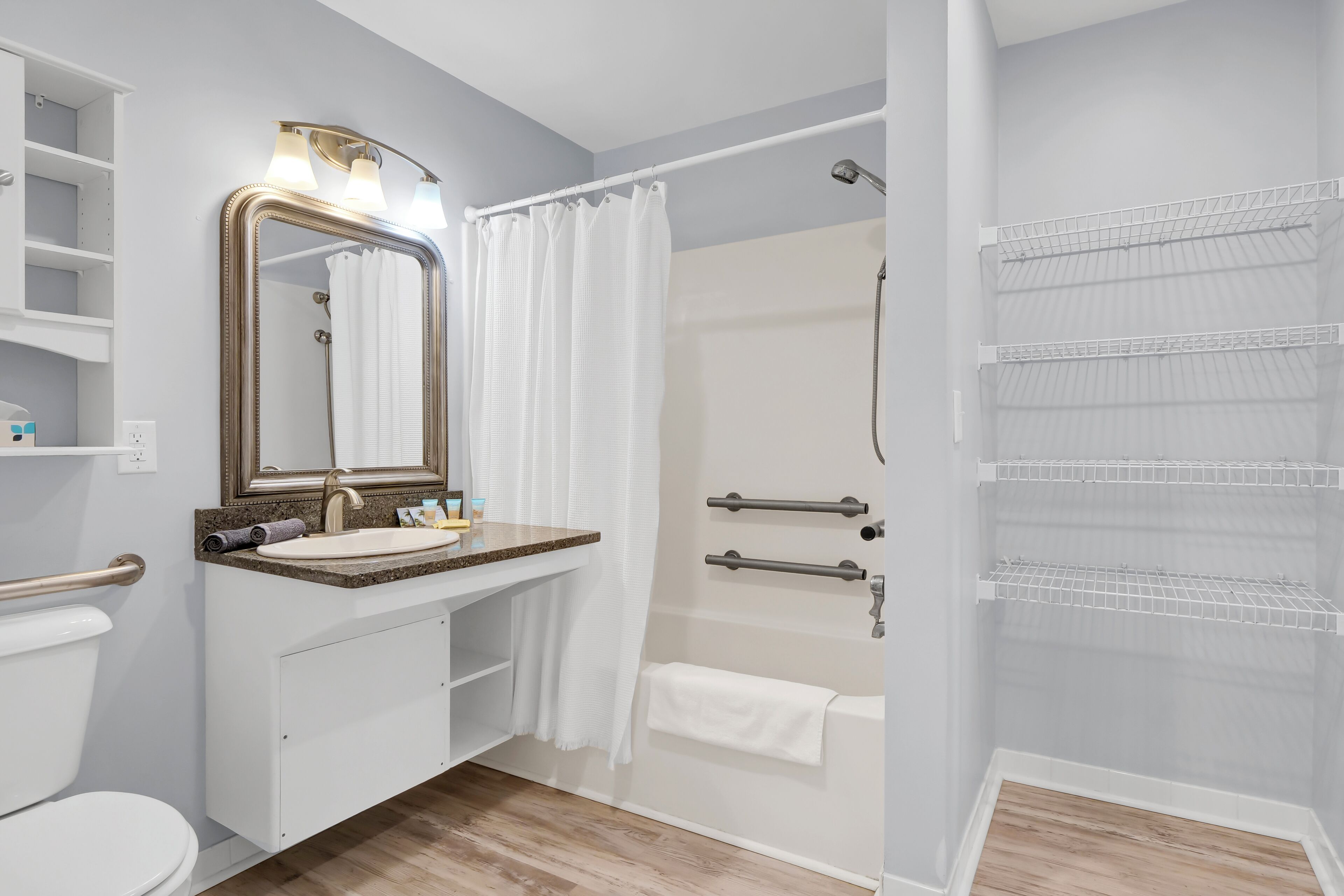 A modern bathroom with a vanity, toilet, shower, and storage shelves.
