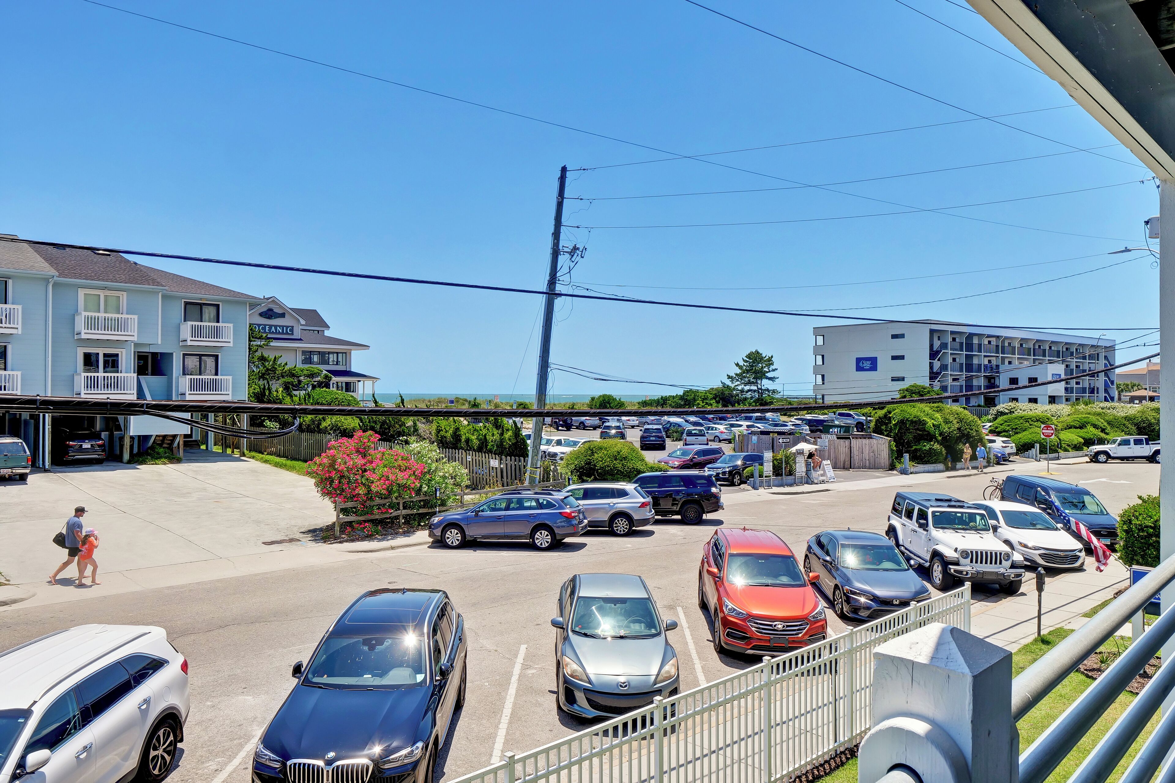 Un parking où sont garées différentes voitures, un bâtiment sur lequel on peut lire l’inscription « Oceanic », et un ciel bleu dégagé.