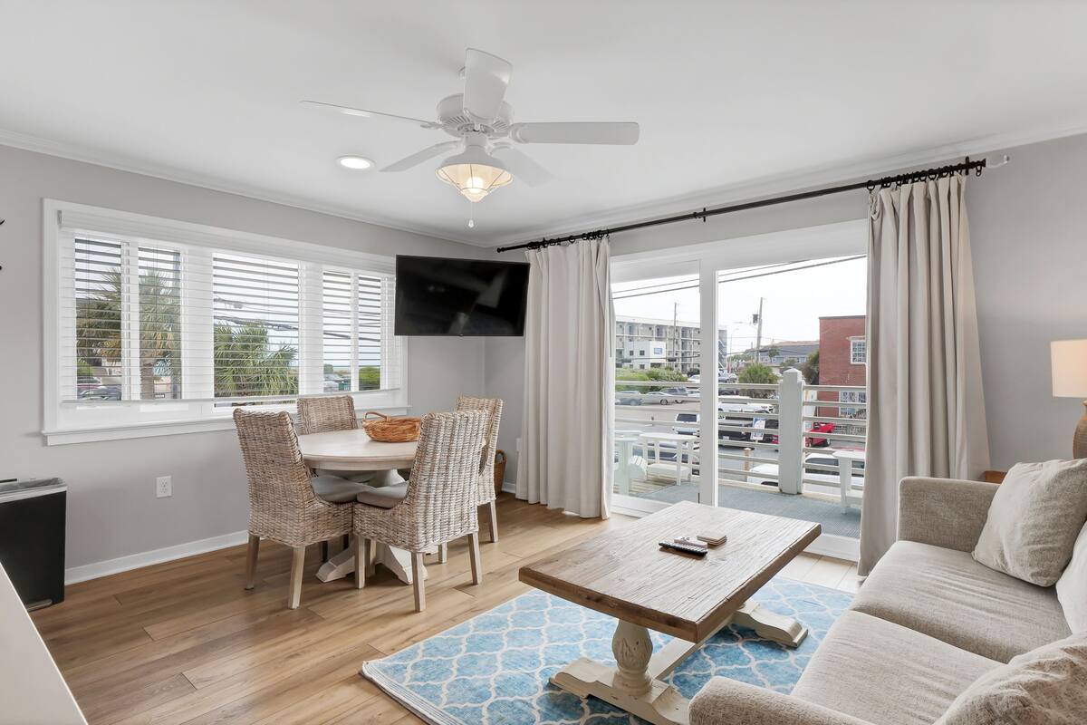 Un salon moderne comprenant un coin repas, un ventilateur de plafond, un téléviseur à écran plat et une grande fenêtre avec des rideaux.