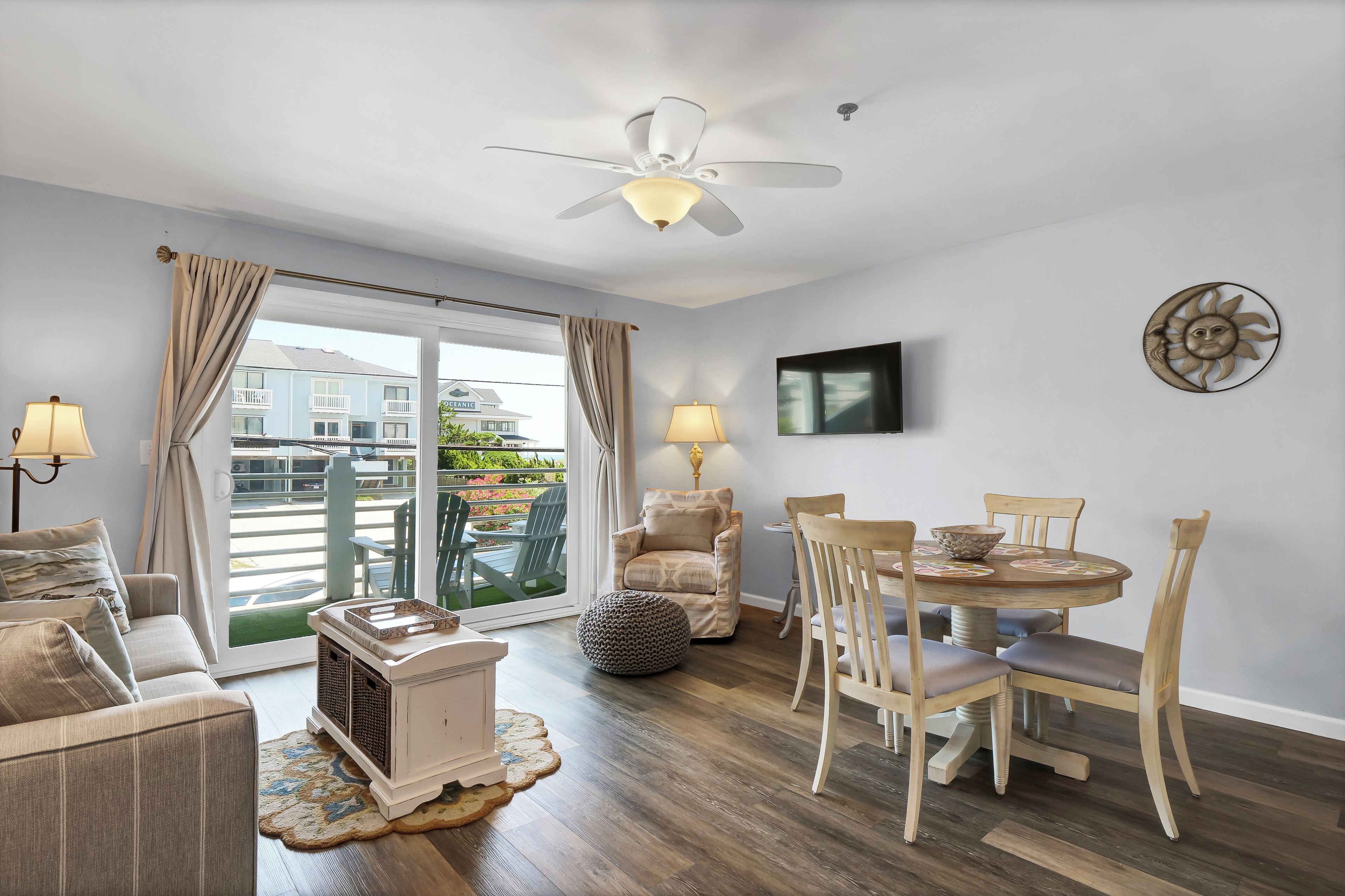 Una sala moderna con sofá, una mesa de comedor con sillas, un ventilador de techo y vistas al balcón exterior.