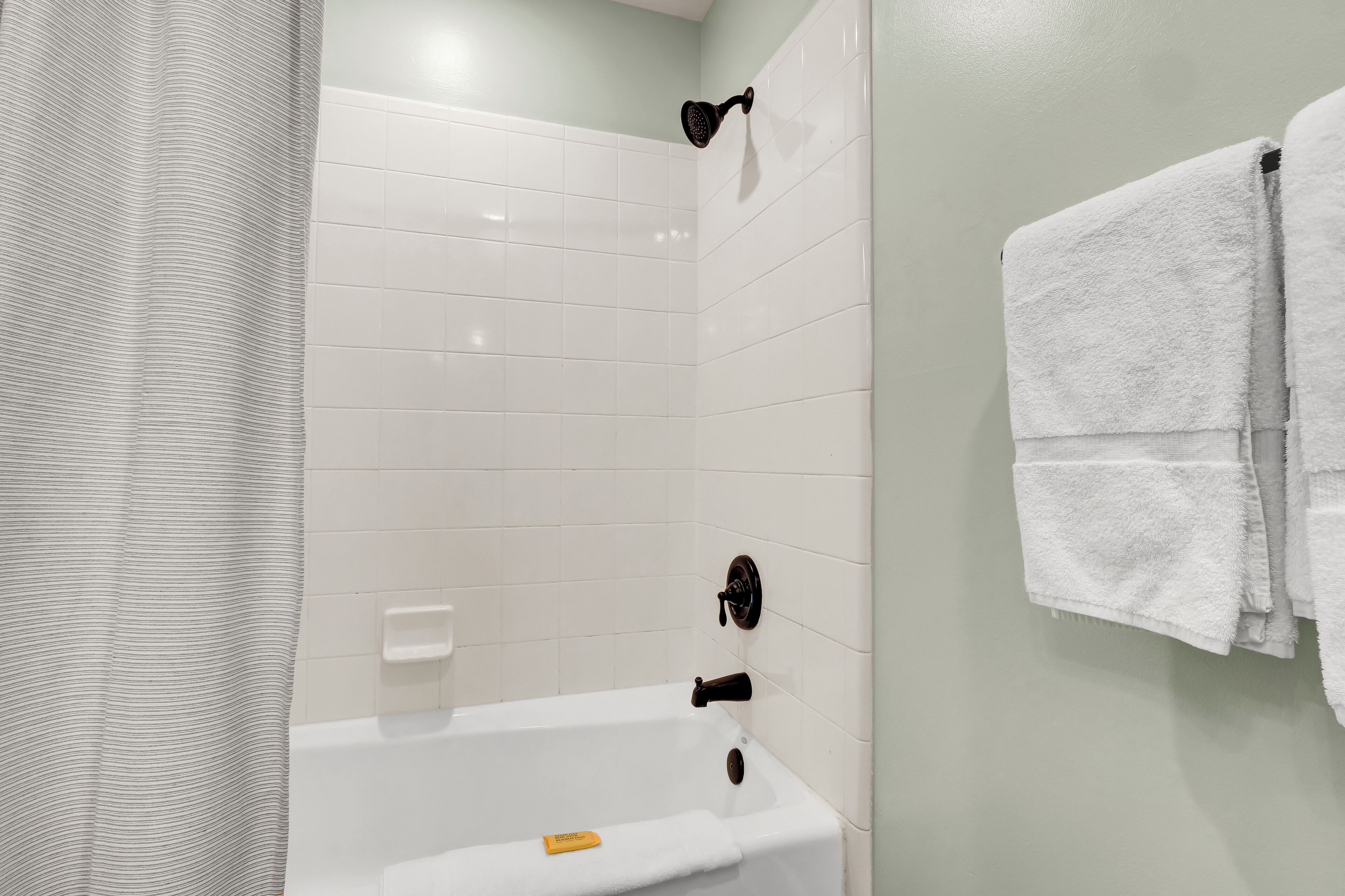A bathroom with a white bathtub, a showerhead, and a towel rack with towels.