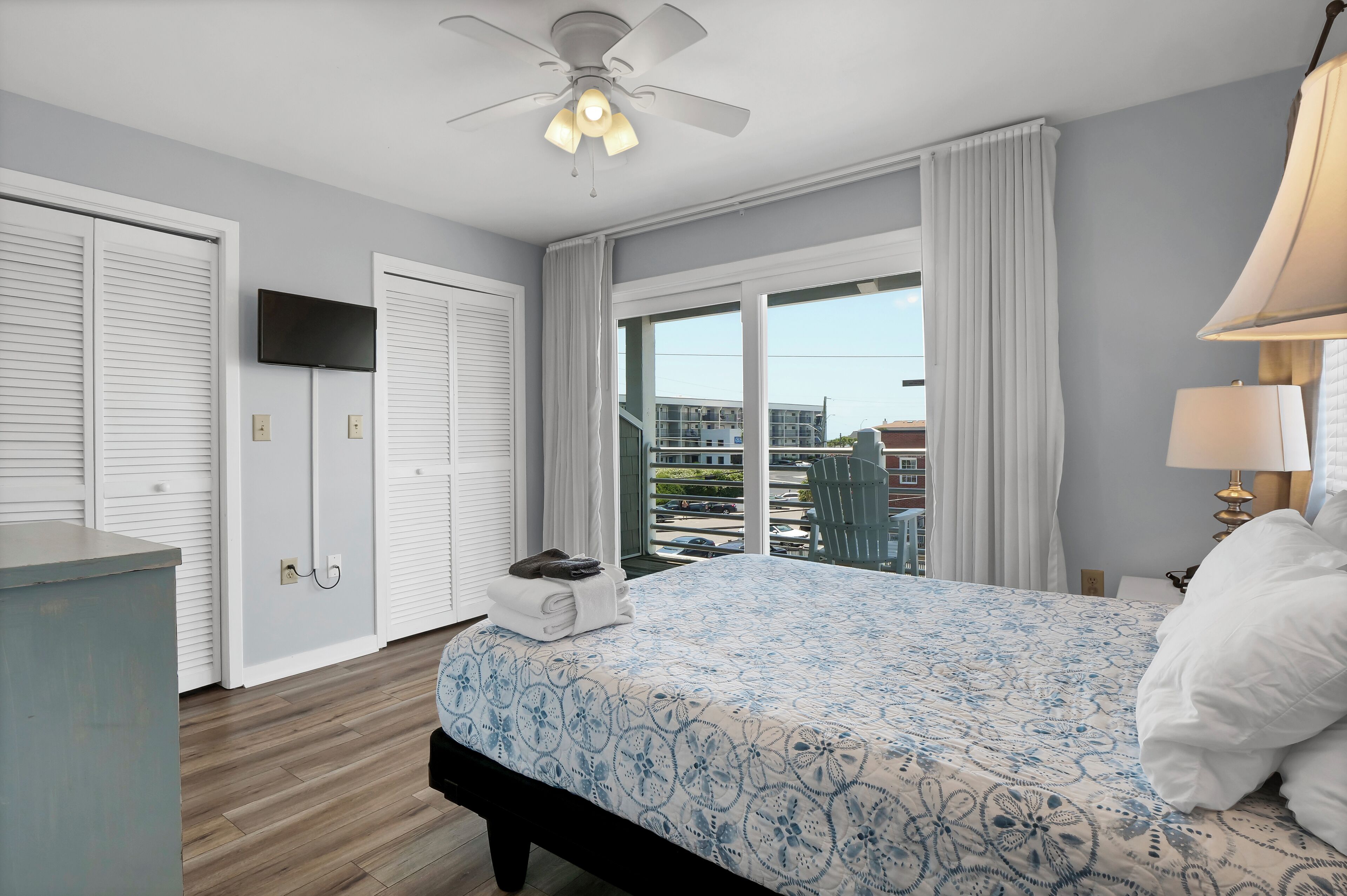 A hotel room with a bed, a ceiling fan, a TV, and a view of the outside.