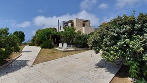 Um edifício moderno com telhado plano e chaminé, rodeado por vegetação exuberante e um caminho pavimentado.