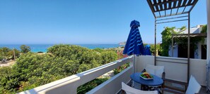 A balcony with a table and chairs, overlooking a coastal view with trees and a clear sky. - Doma Apartments (Kissamos)