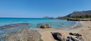 A beach with clear turquoise water, rocky foreground, and a mountainous backdrop. - Doma Apartments (Kissamos)