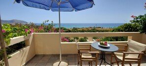 A balcony with a table and chairs, a blue umbrella, and a view of the sea. - Doma Apartments (Kissamos)